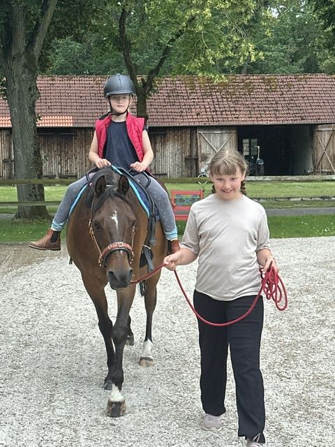 Ein Kind mit Helm reitet, ein Mädchen führt das Pony