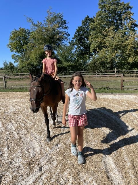 Ein Kind reitet auf dem Reitplatz, ein anderes zeigt den Daumen hoch